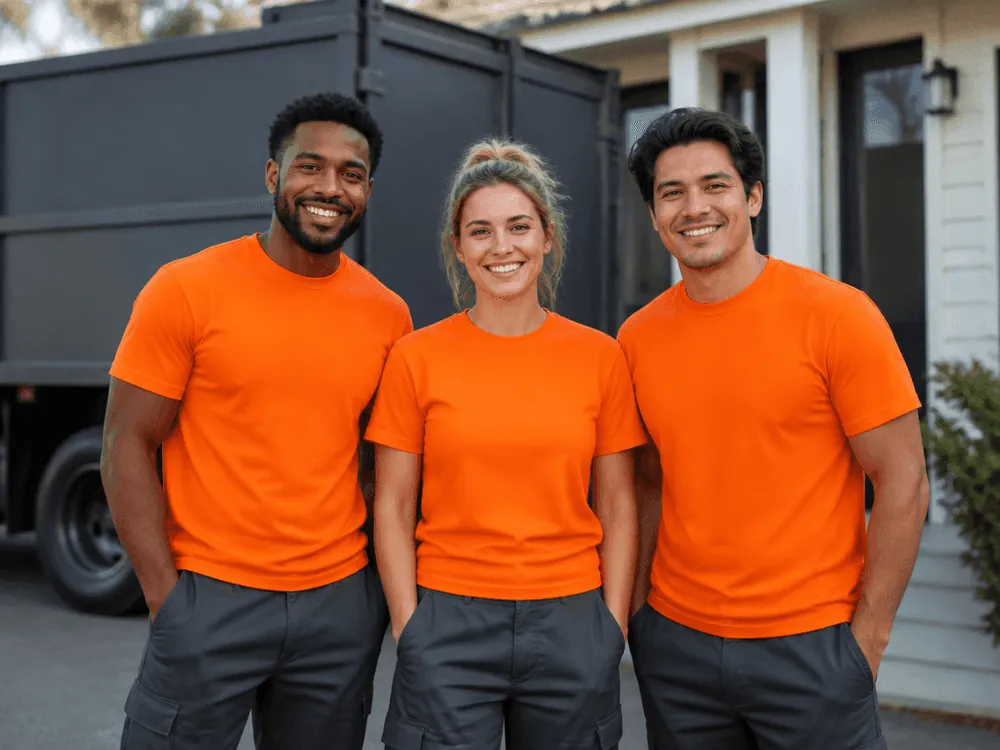 Three crew members in orange shirts smiling in front of a truck