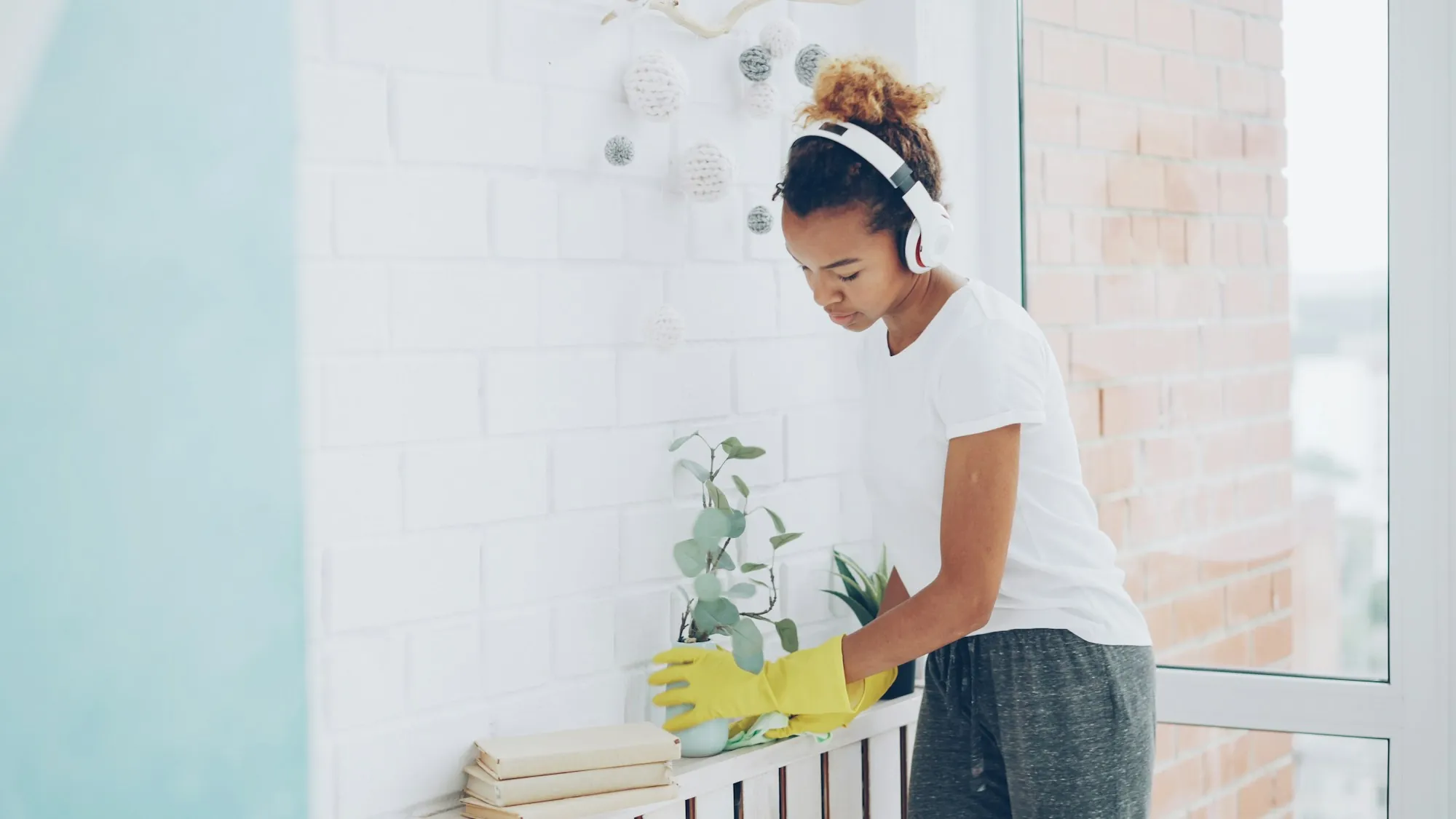 A cleaner in yellow gloves wiping down a white shelf by a bright window
