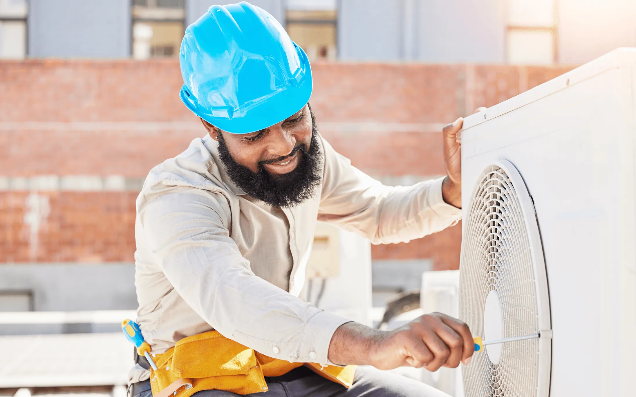 A technician in a blue hard hat servicing an outdoor unit