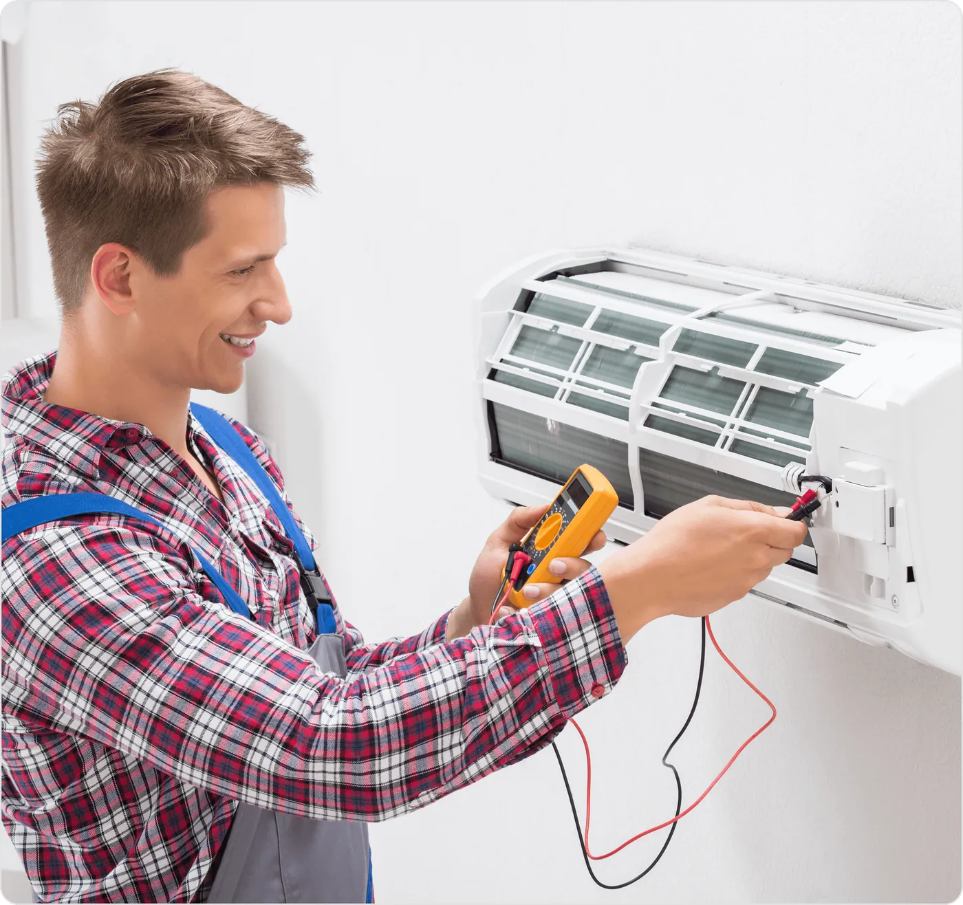 A smiling technician testing an indoor unit with a multimeter
