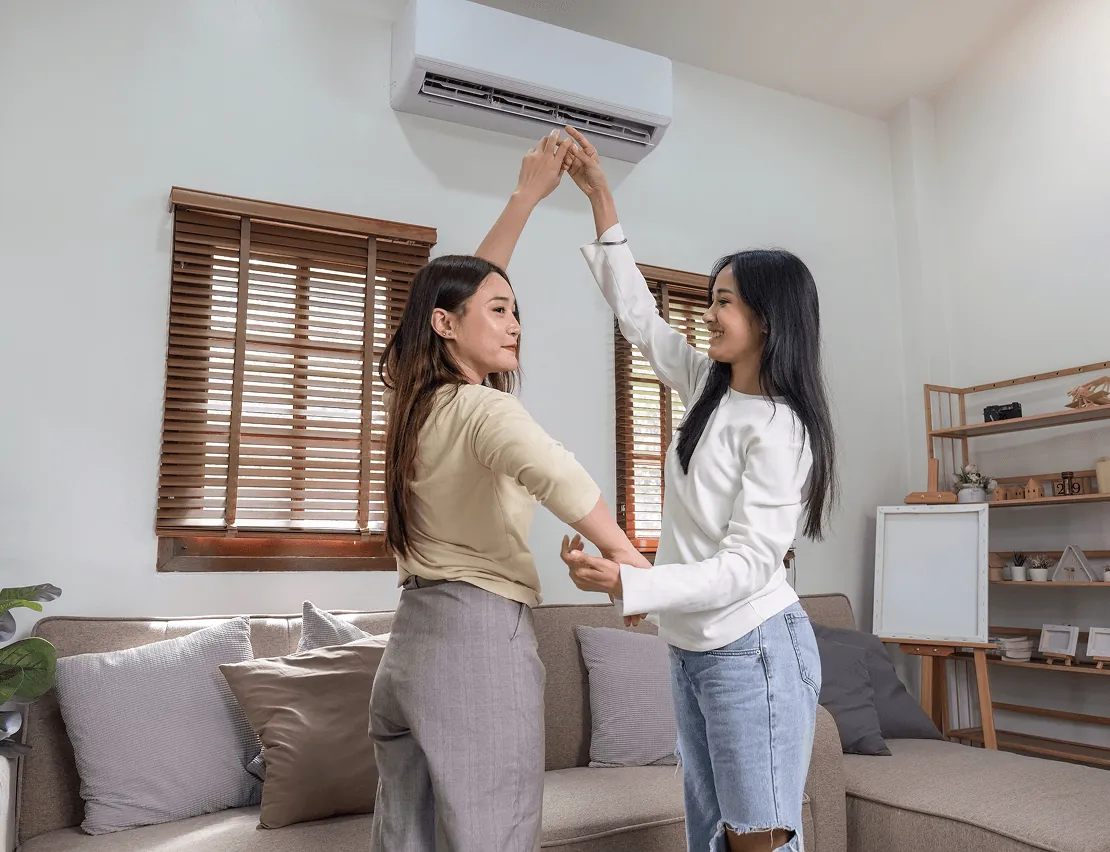 Two women adjusting a wall air conditioner at home