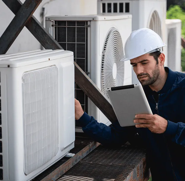 A technician in a hard hat checking outdoor units on a tablet