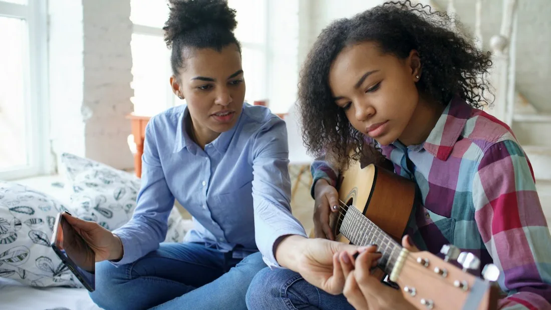 A teacher and a teenage student sitting together with a guitar