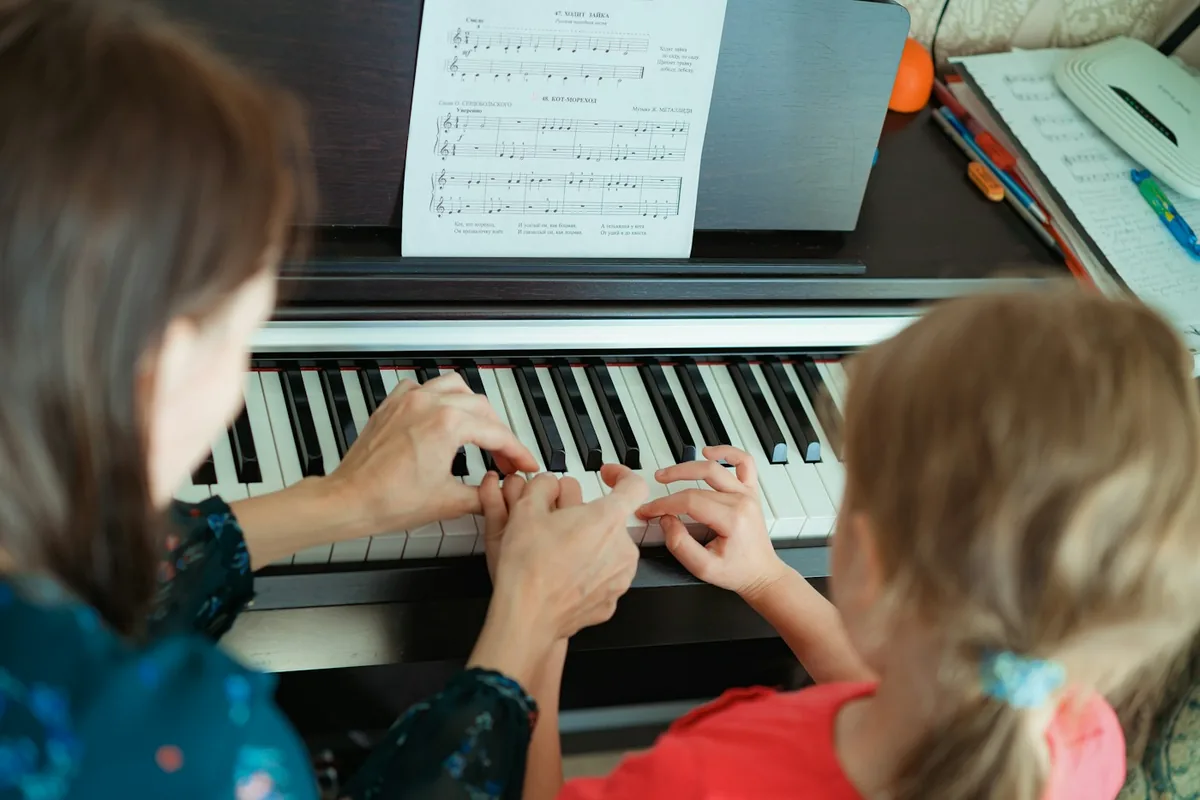 A piano teacher showing a young girl where to put her hands on the keys