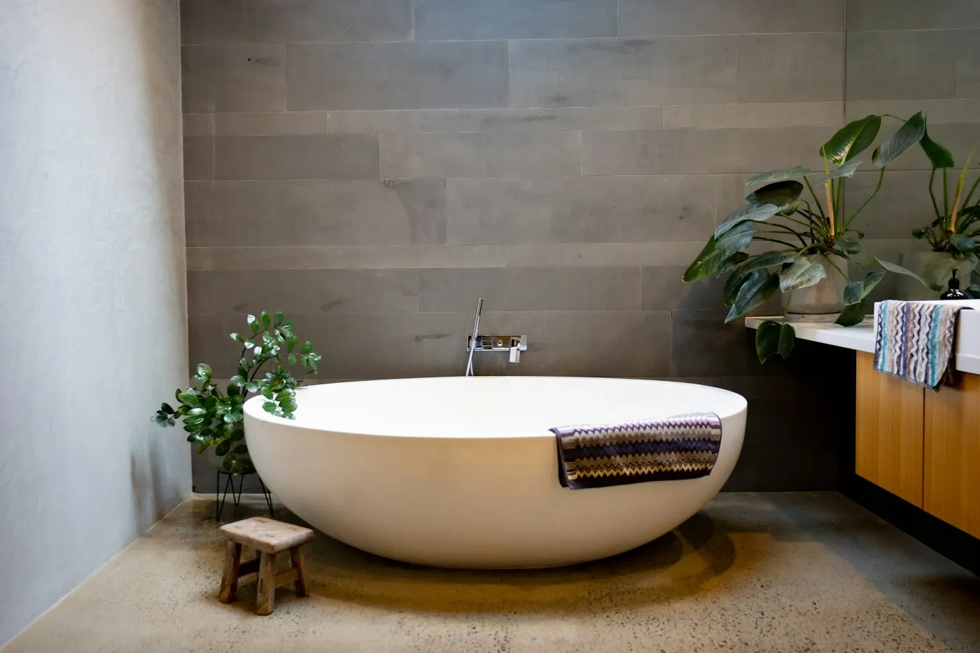 A freestanding bathtub with a floor-mounted tap in a bathroom with wood-look walls
