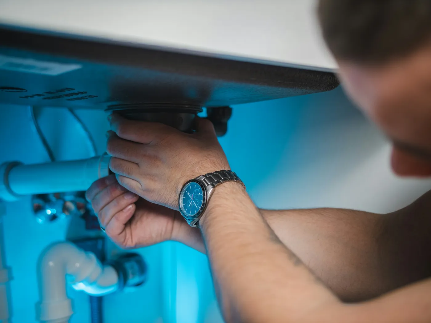 A plumber tightening a pipe fitting under a sink
