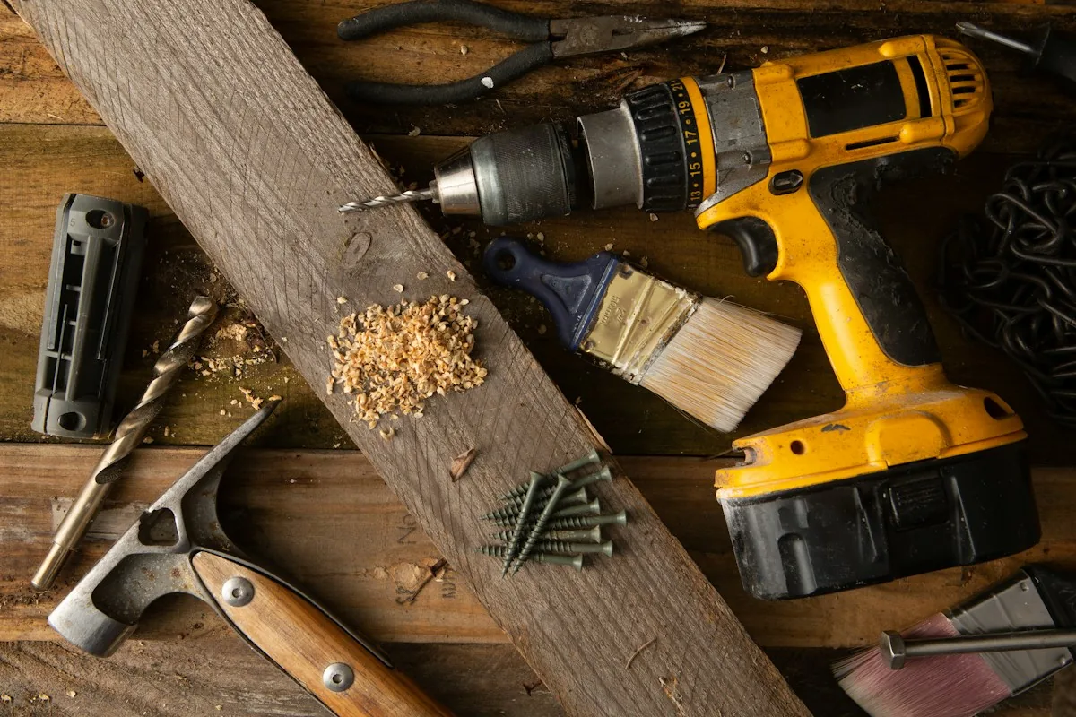 A cordless drill, a brush and screws on a timber board