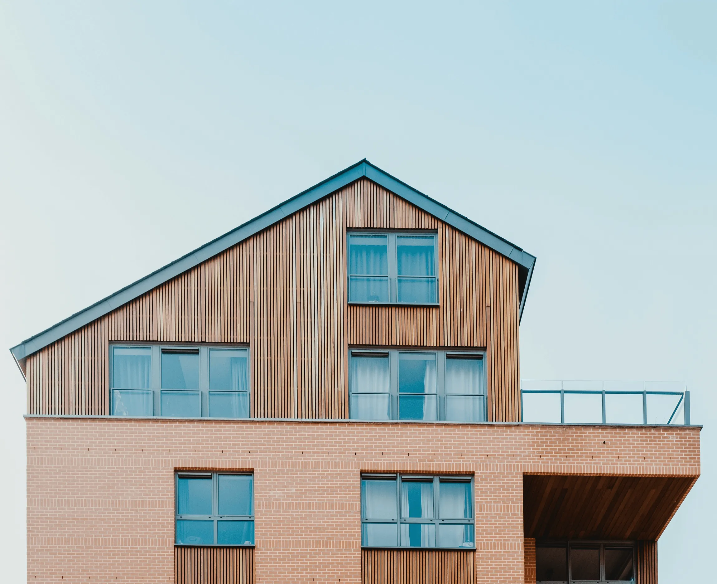 A timber-clad house above a brick base against a pale sky