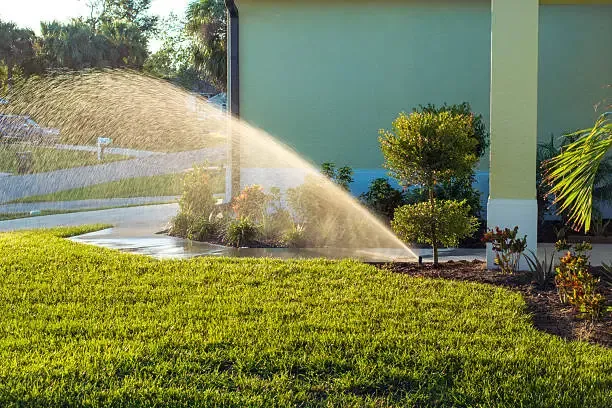 A sprinkler arcing water over a lawn beside a house