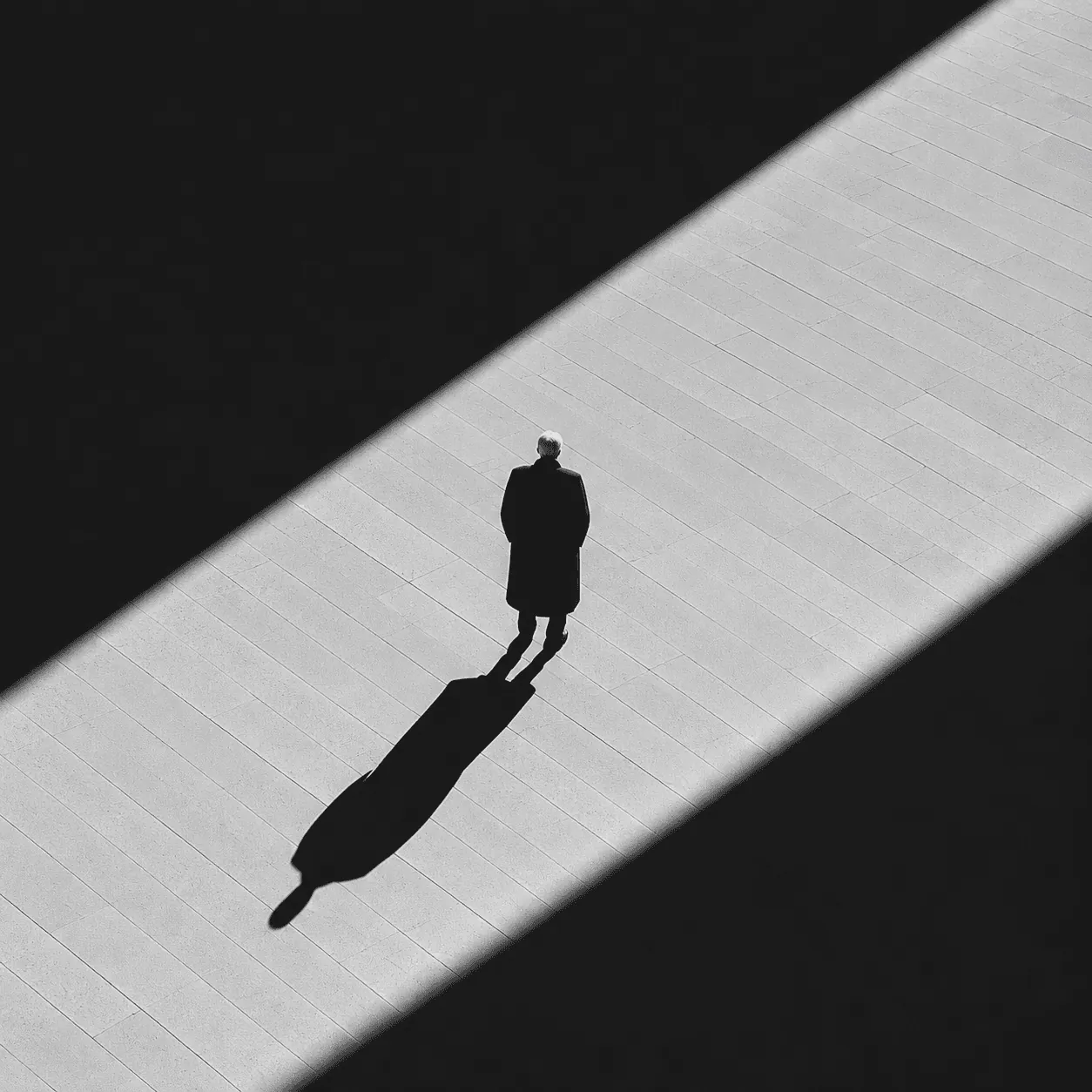 A man in a long coat casting a long shadow