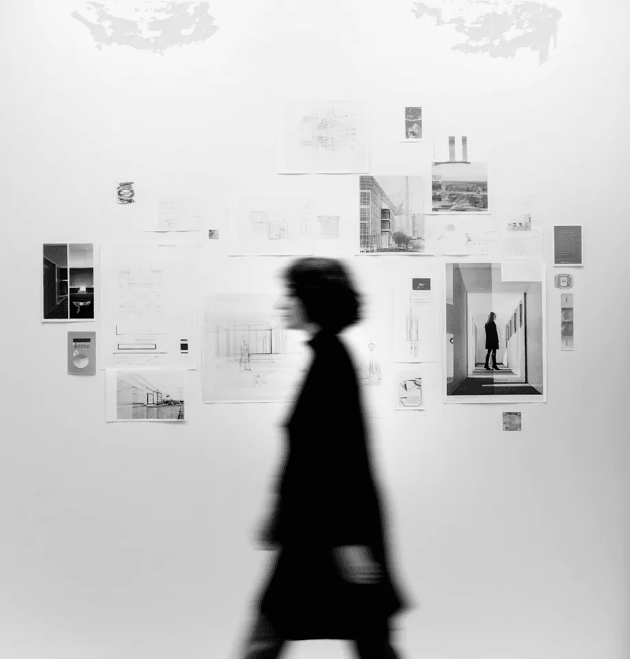 A woman passing a wall of pinned drawings