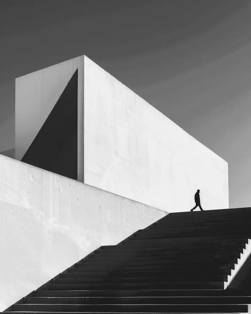 A small figure climbing steps beside a white concrete volume