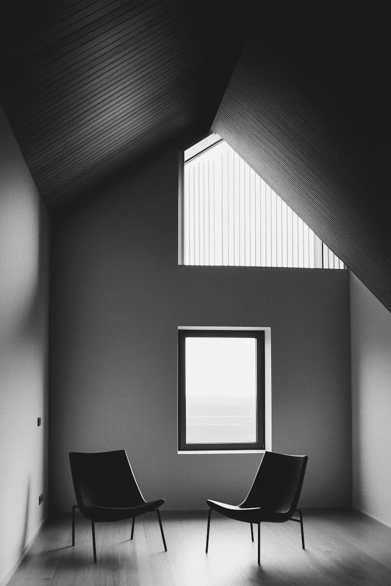 Two black chairs by a window in a grey room