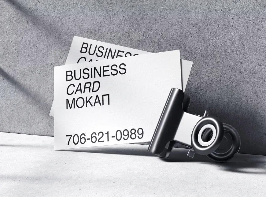 Business cards beside a camera lens on grey concrete