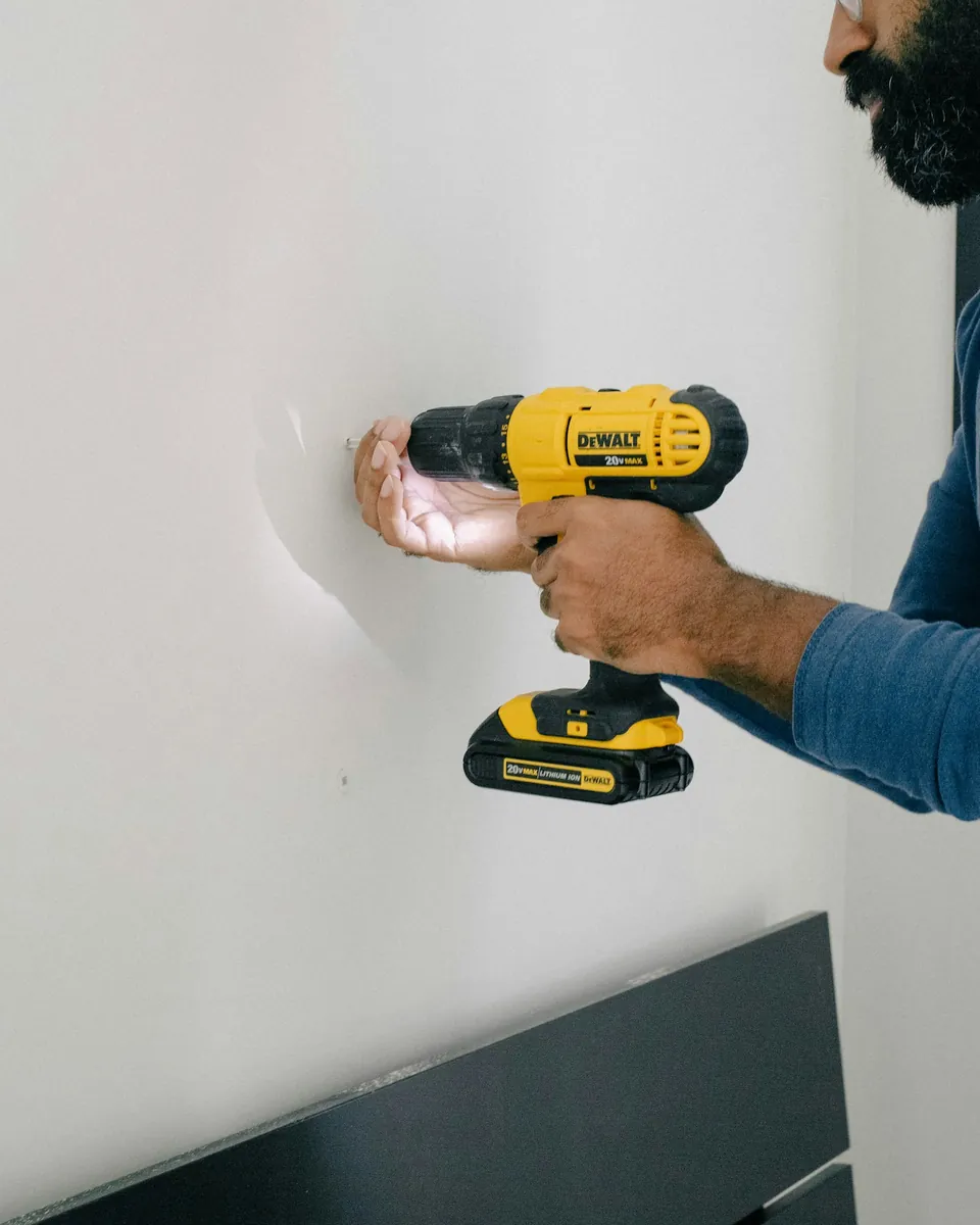 A hand drilling into a white wall
