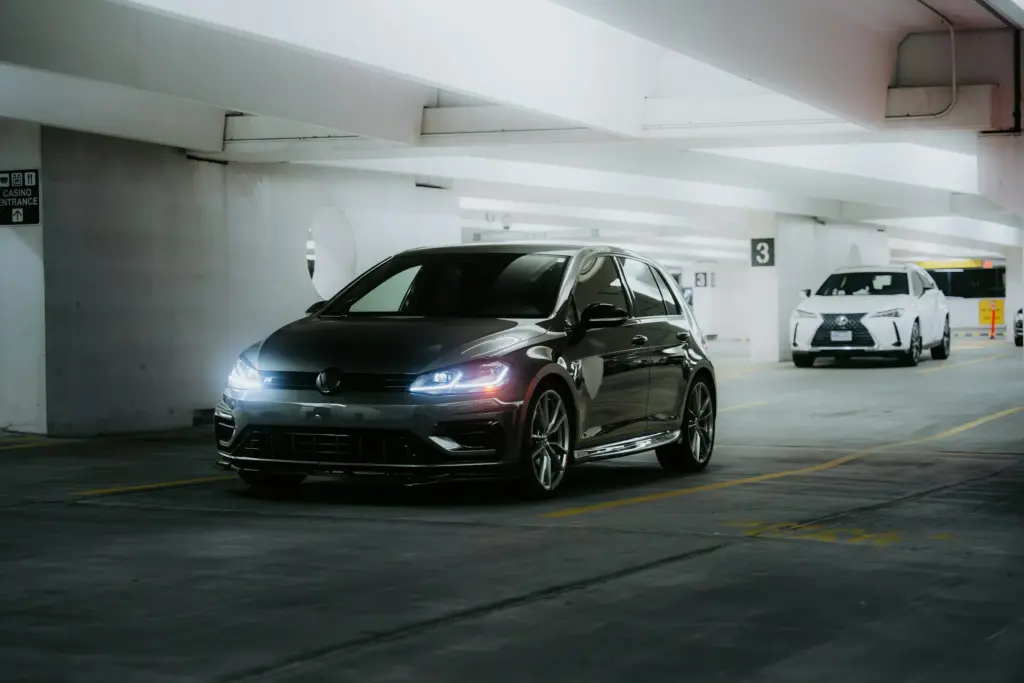 A black hatchback with its headlights on in a parking garage