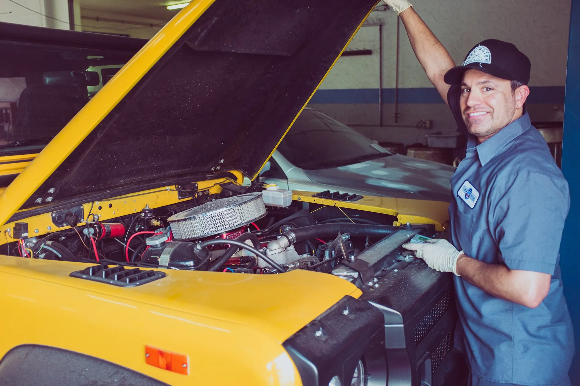 A smiling mechanic at the open bonnet of a yellow car