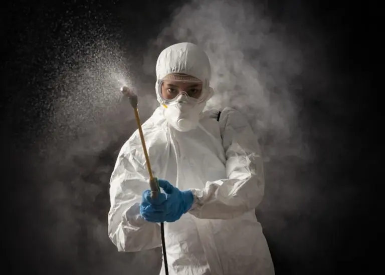 A technician in a white suit spraying in the dark