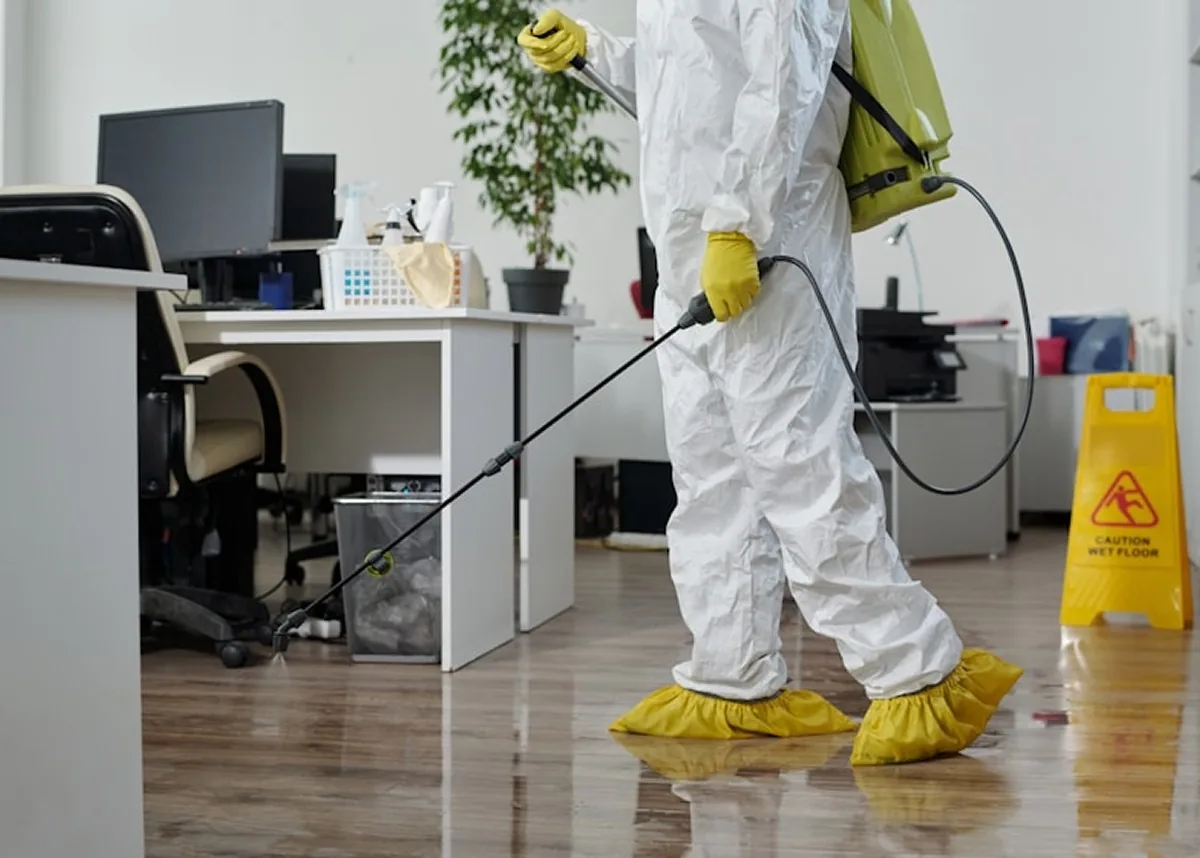 A technician in a protective suit spraying an office floor