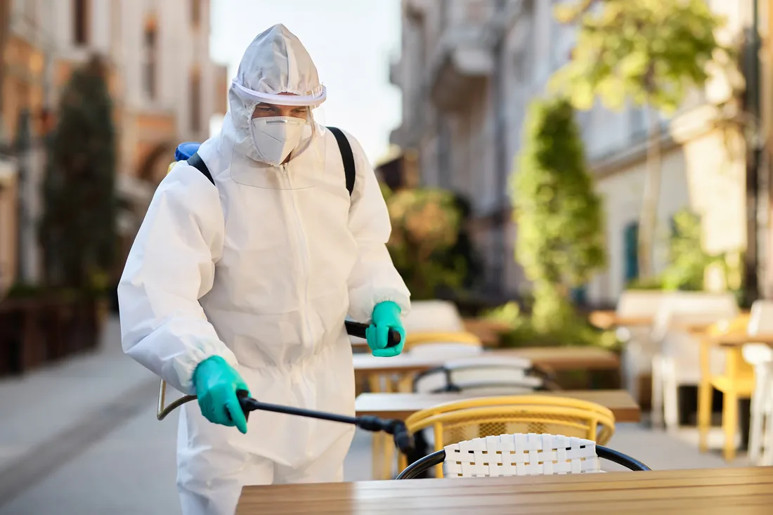 A technician in a white protective suit disinfecting a cafe terrace