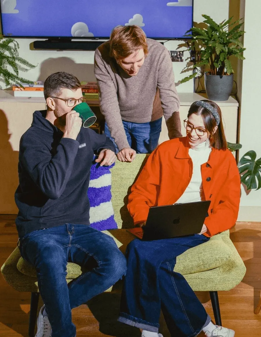 Three colleagues talking over a laptop on a sofa in a bright office