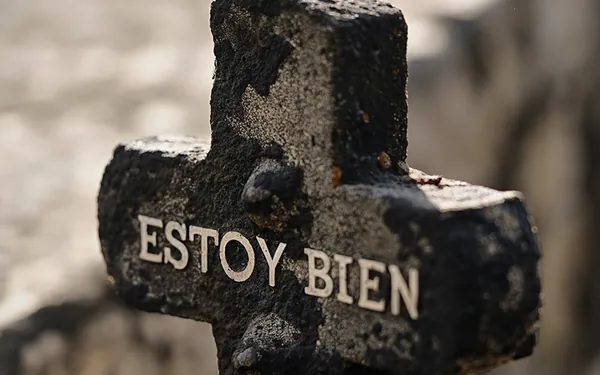 A dark stone cross with the words Estoy Bien carved into it
