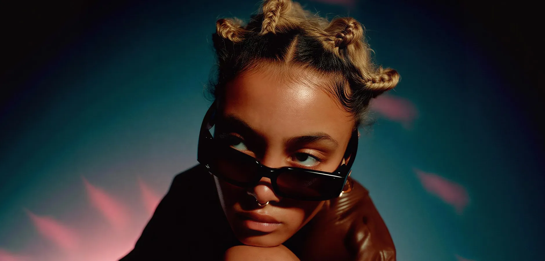 A young woman with braided buns looking over dark sunglasses