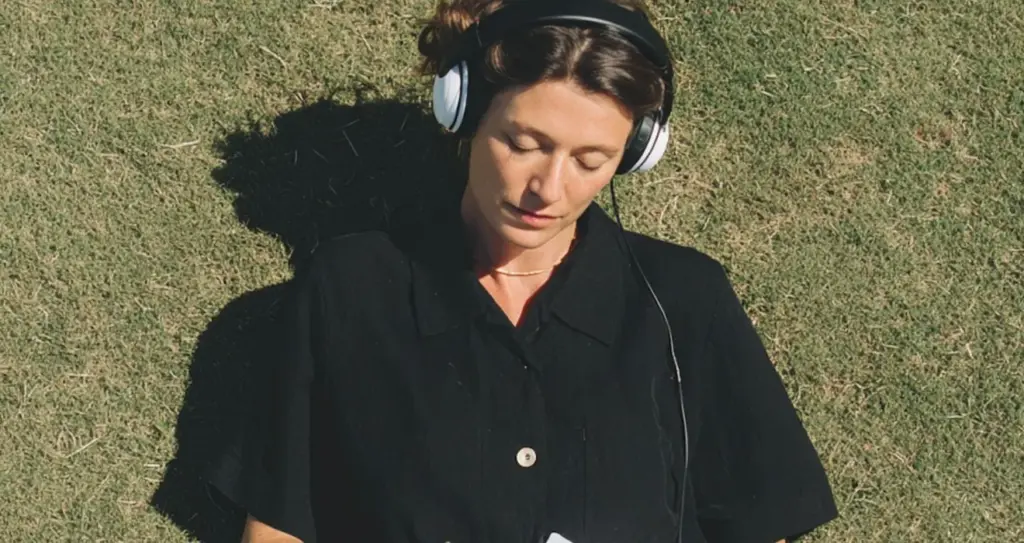 A woman with headphones writing on paper, lying on the grass