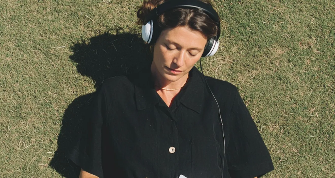 A woman with headphones writing on paper, lying on the grass