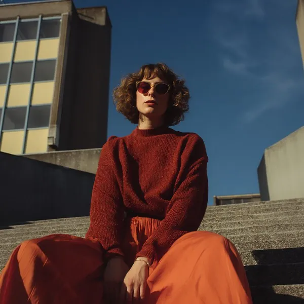 A woman in a red jumper and sunglasses sitting on concrete steps