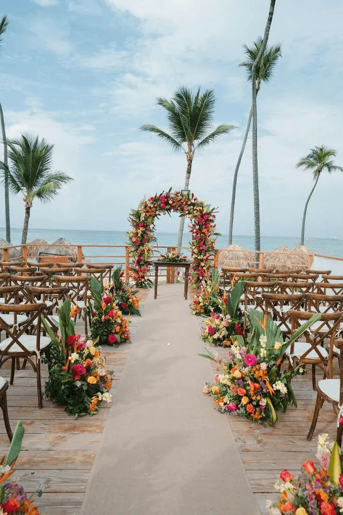 A beach wedding aisle leading to an arch of tropical flowers