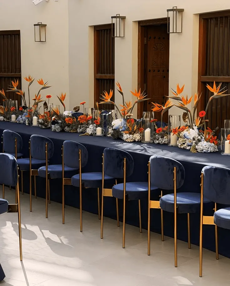 A long dinner table with navy chairs and bird-of-paradise arrangements
