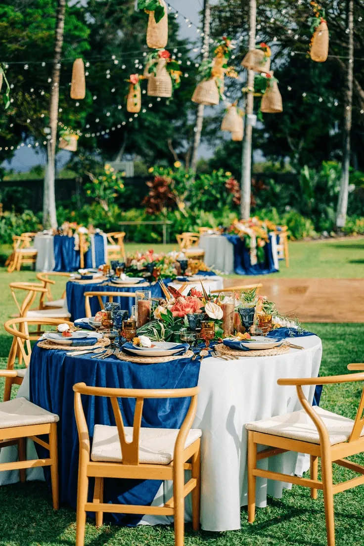 Round tables with blue cloths and flowers in a lantern-lit garden