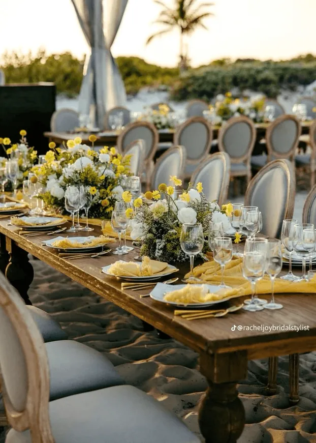 A long table with yellow flowers under a sail awning