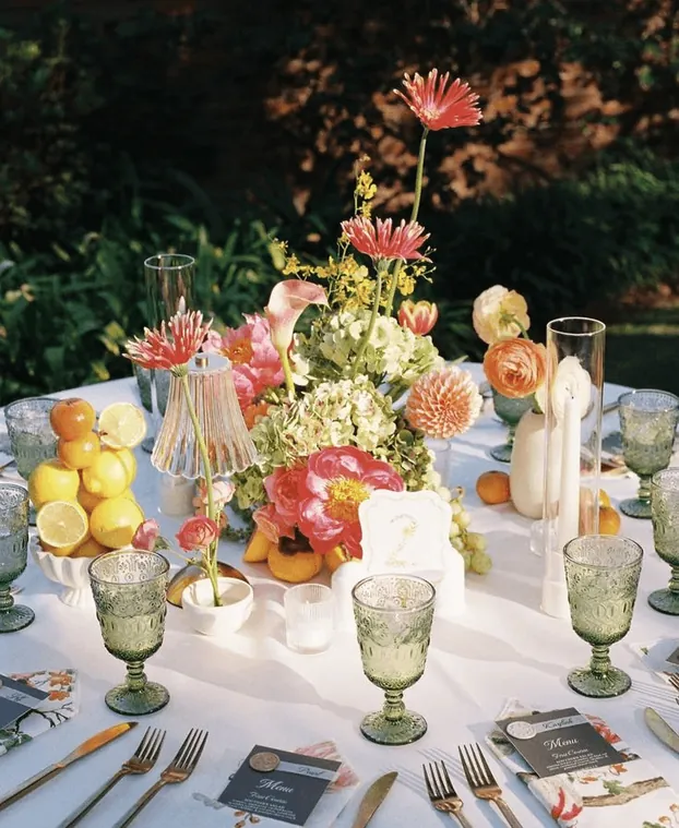 A round table set with lemons, glassware and bright flowers