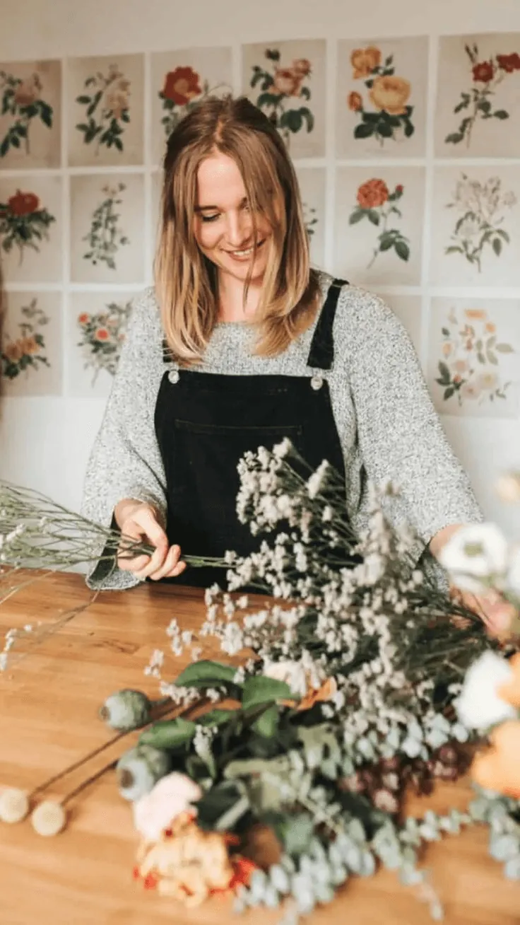 A florist smiling over a bunch of dried flowers at her workbench