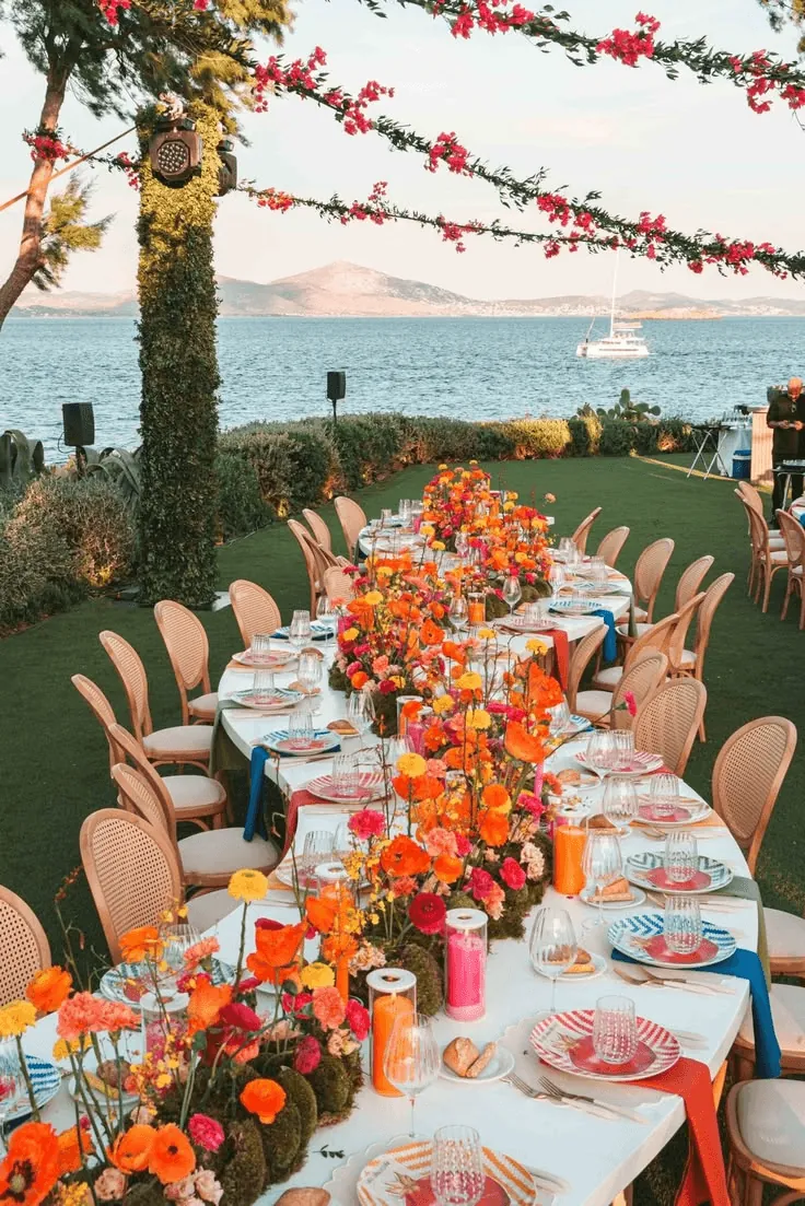 A long seaside table dressed with orange and pink flowers