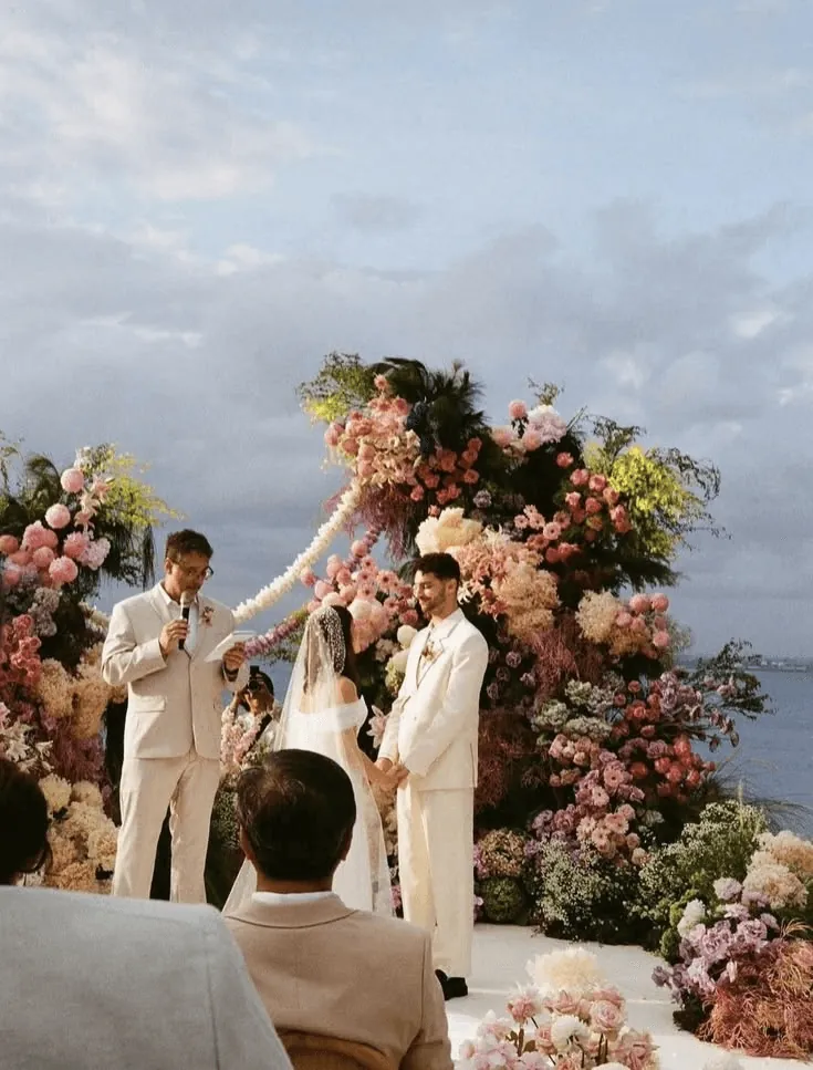 A couple exchanging vows before a floral arch by the sea