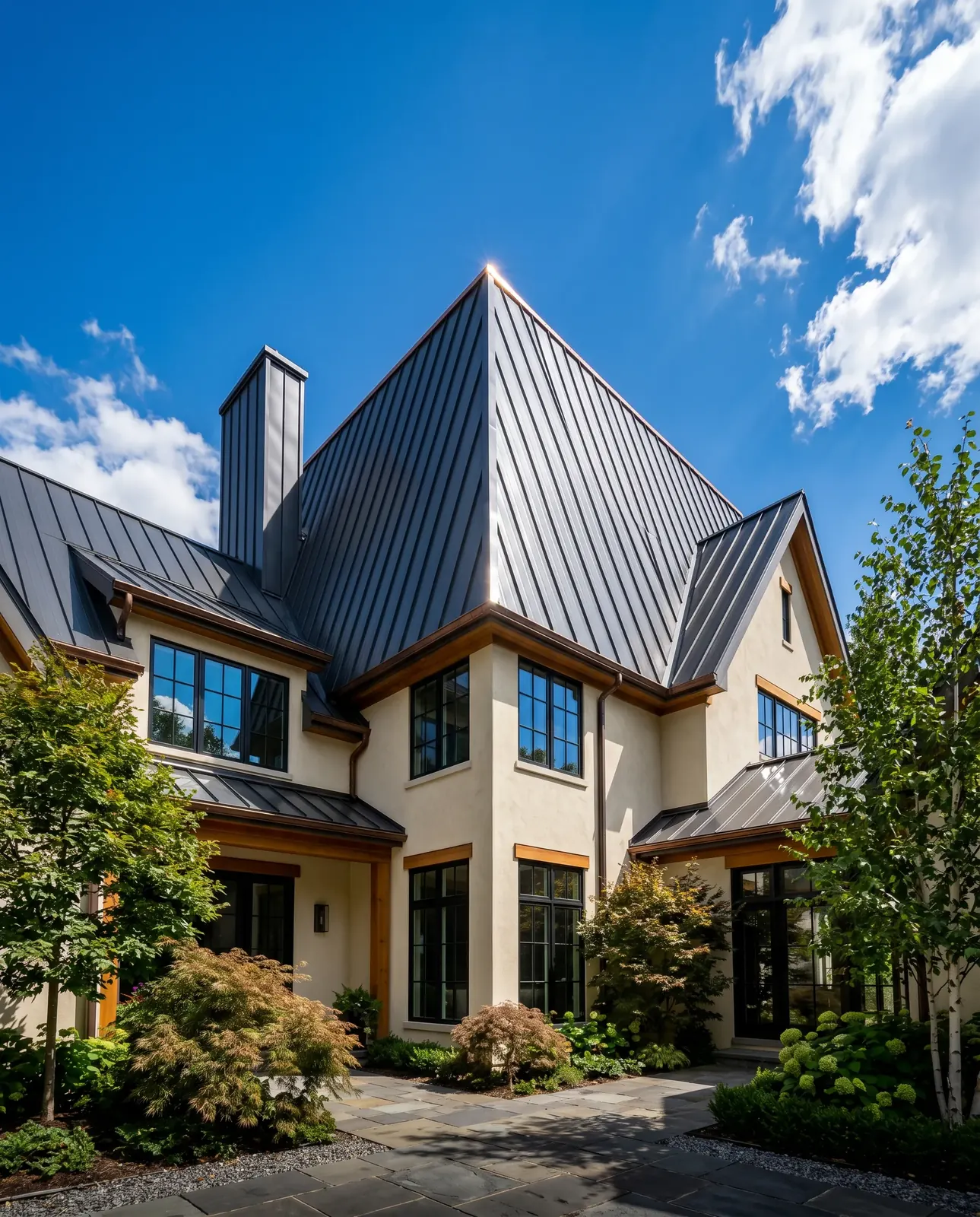 A modern house with a dark grey metal roof and light stucco walls