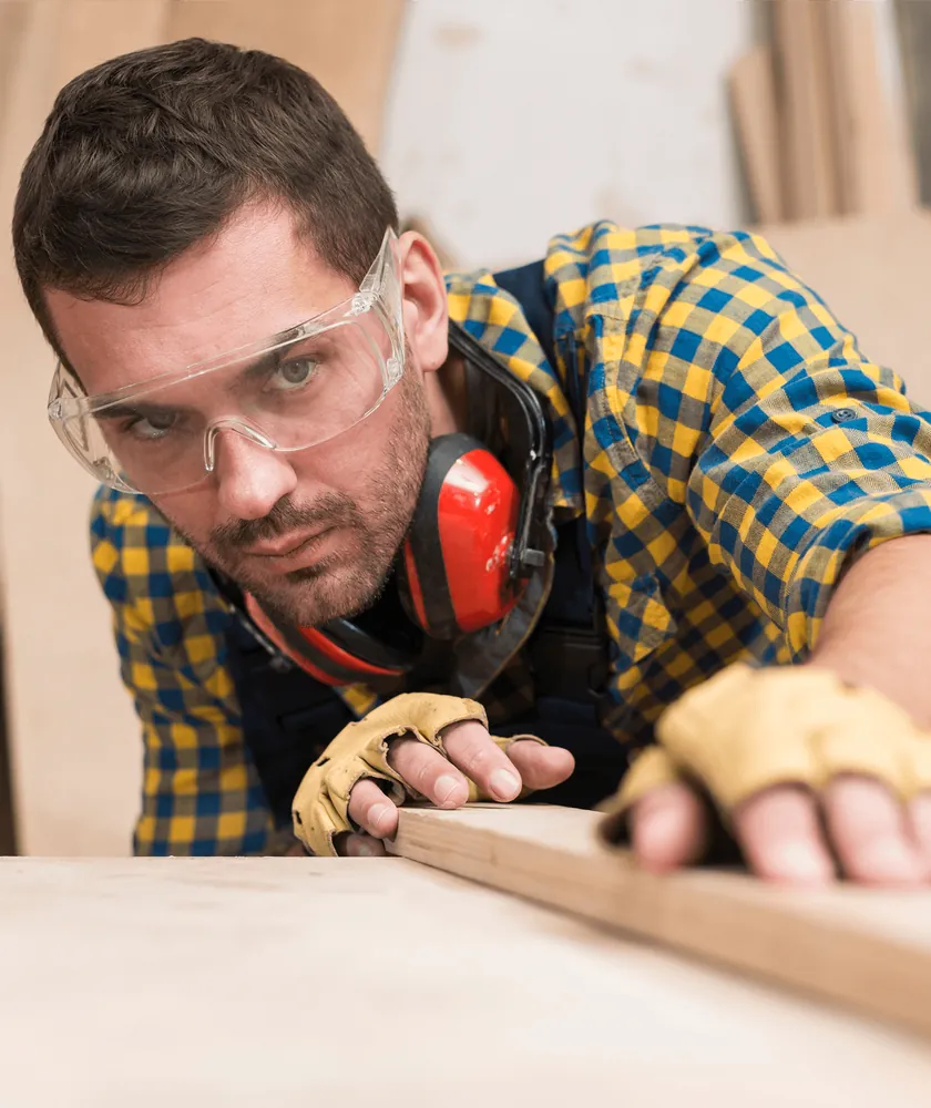 A carpenter in safety glasses and ear defenders working a wooden board