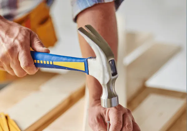 A hand driving a nail into a board with a hammer