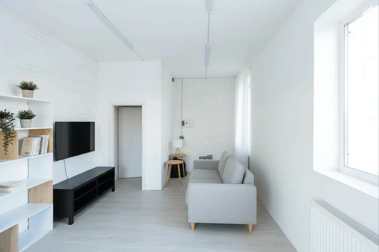A finished white living room with a grey sofa and a TV wall
