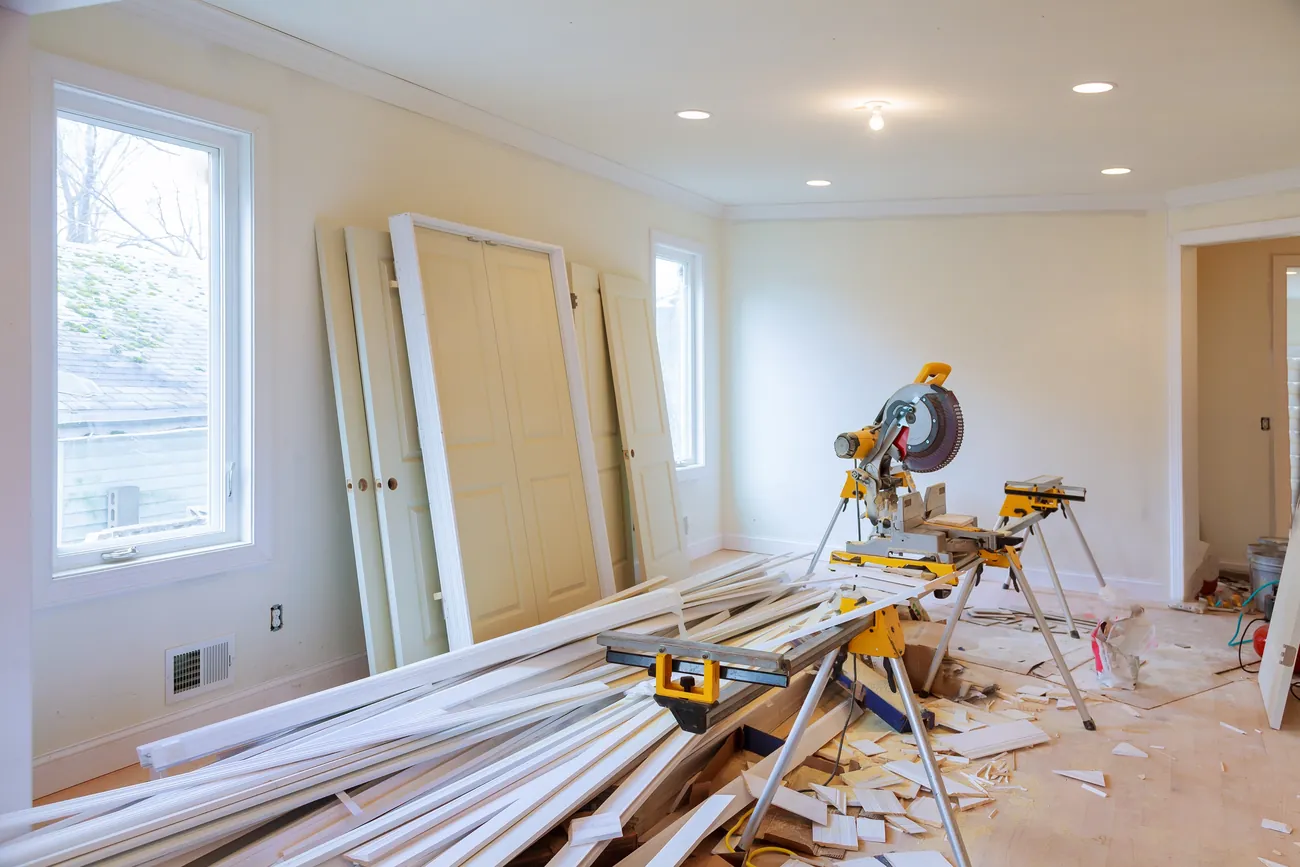 A room under renovation with new doors against the wall and a mitre saw on its stand