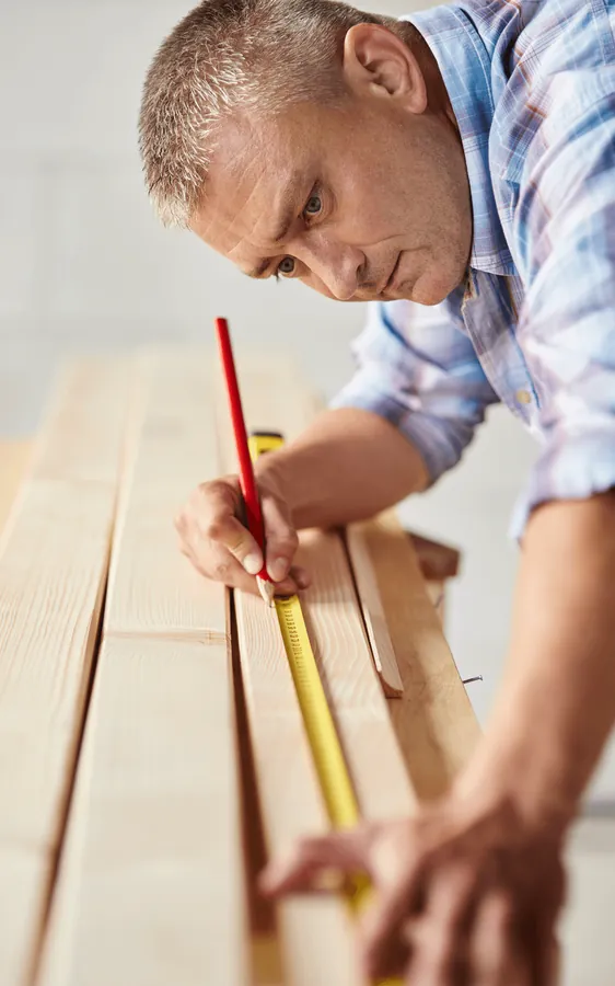 A craftsman measuring a plank with a tape measure and pencil