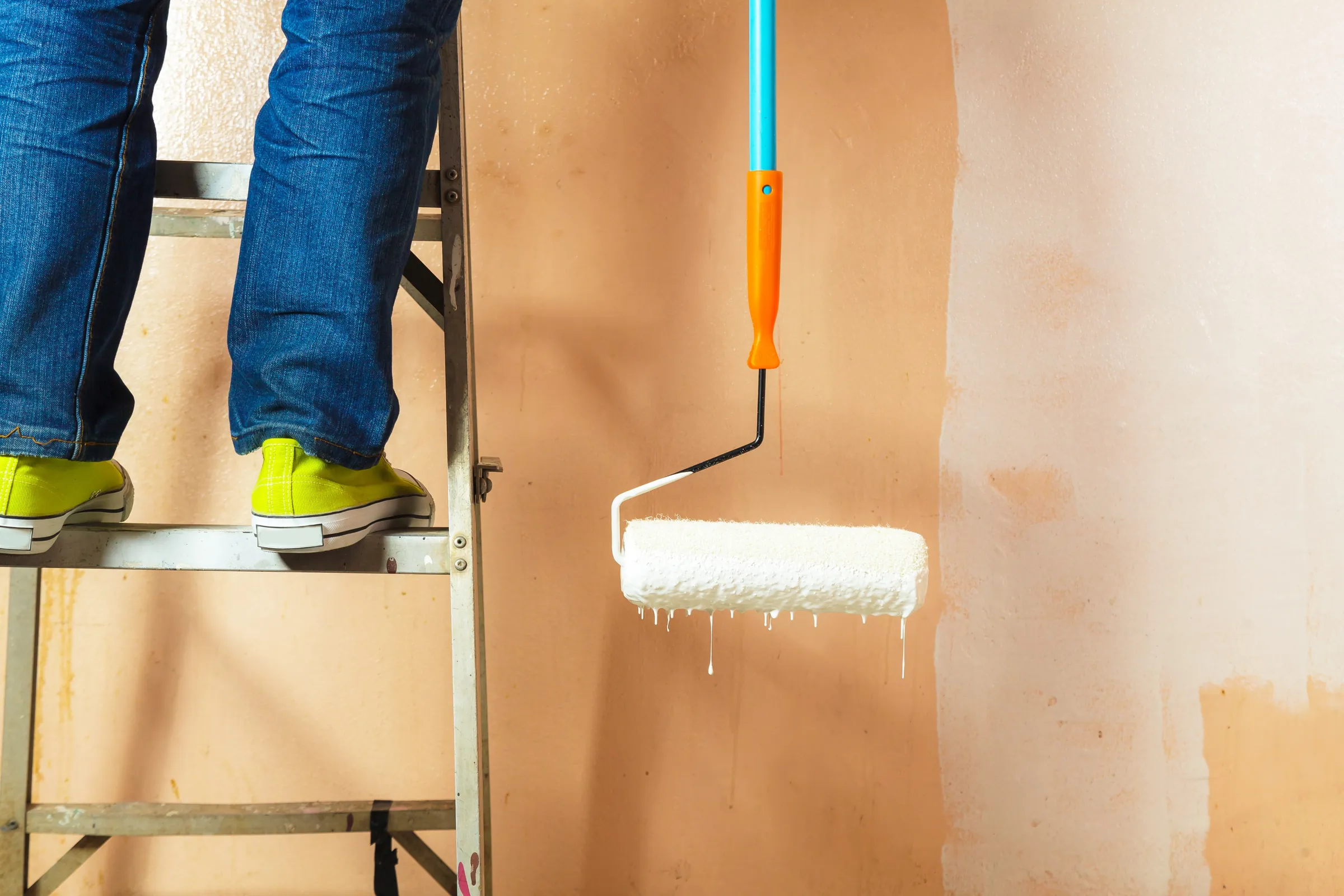 A painter on a stepladder rolling white paint onto a wall