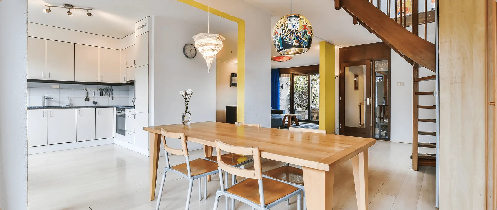A dining room with a wooden table, a colourful pendant lamp and a staircase