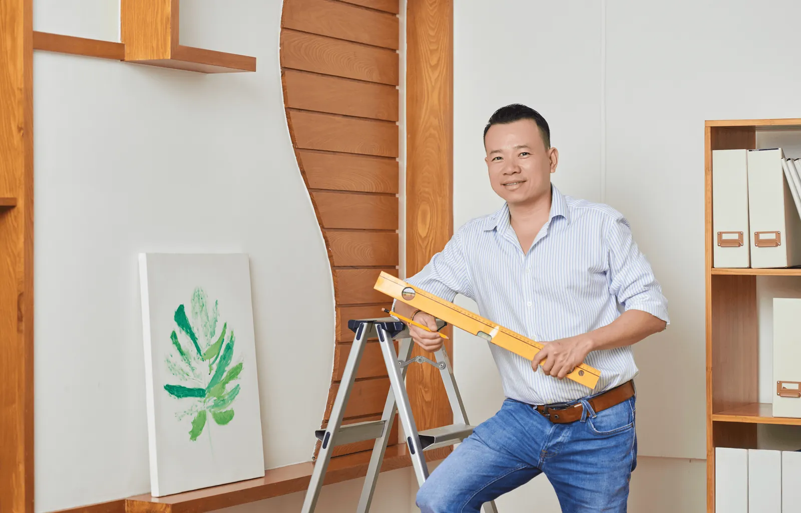 A carpenter holding a spirit level beside a stepladder