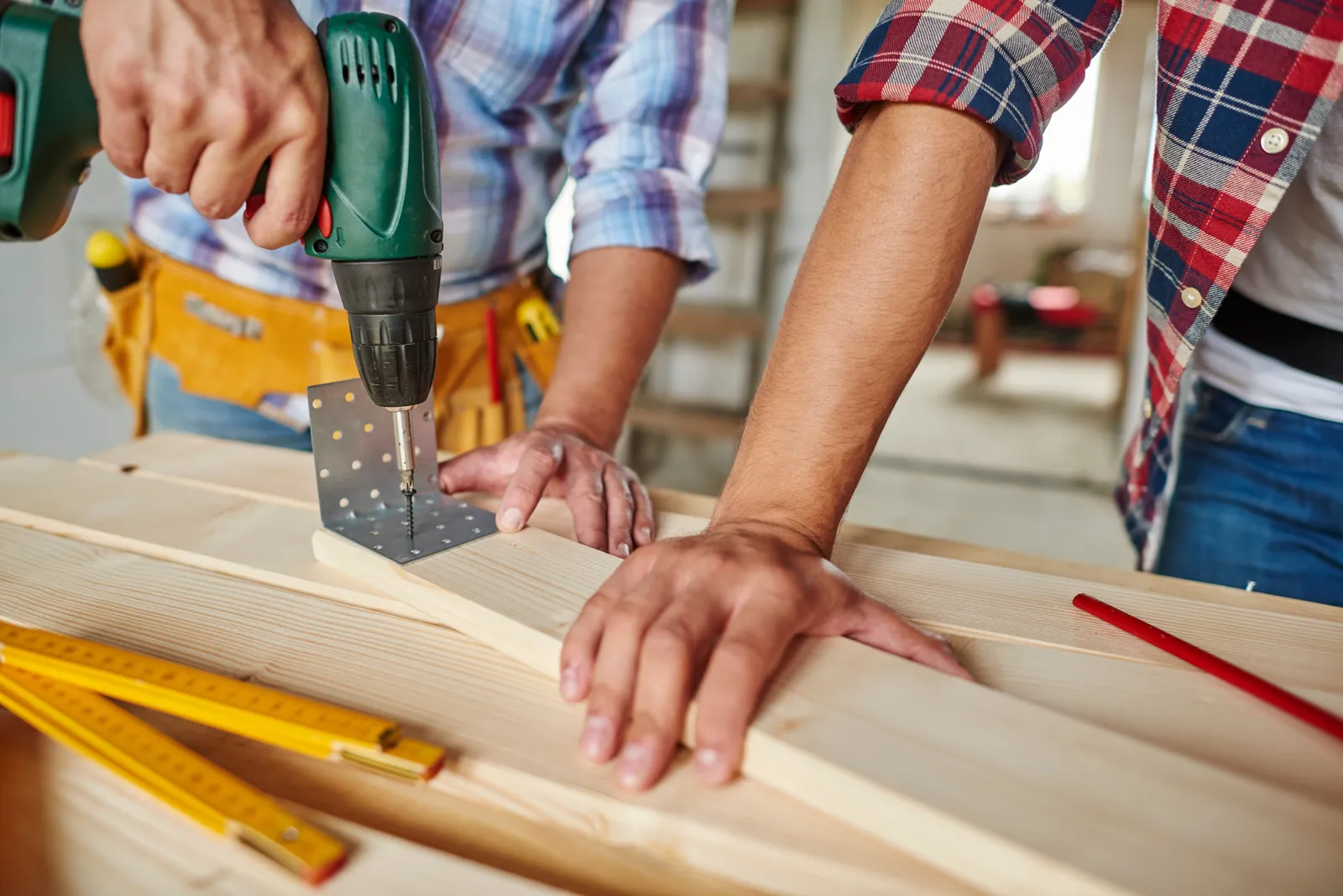 A carpenter drilling a metal bracket into a timber beam