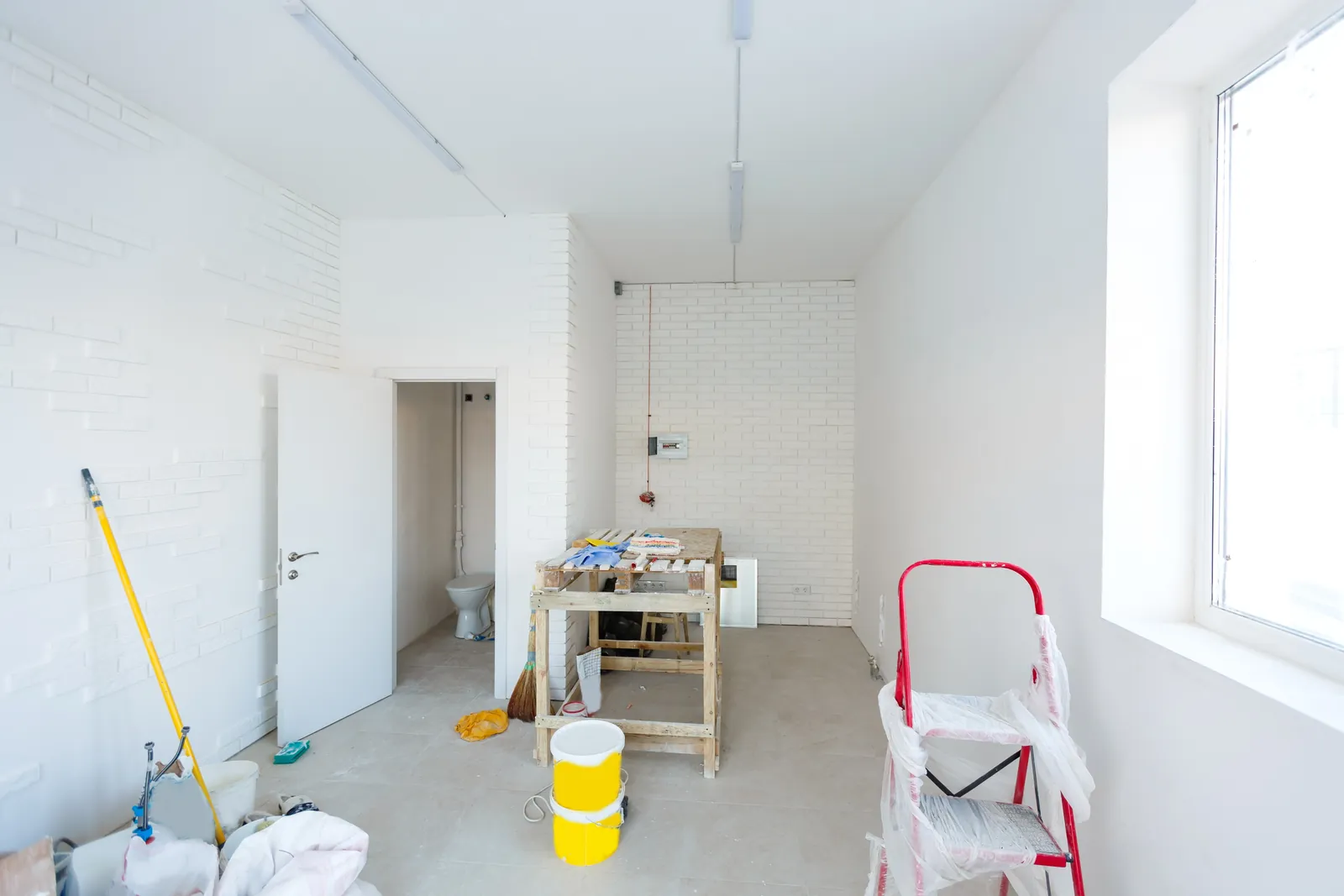 An empty white room with a mop, a paint bucket and a stepladder