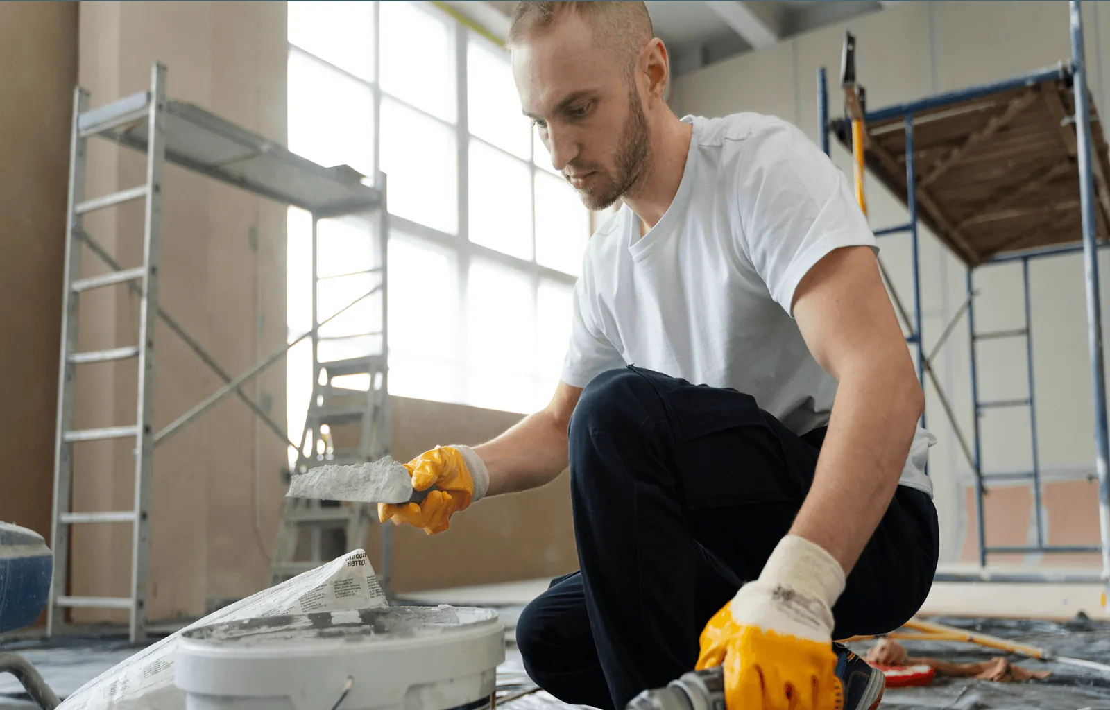 A worker in gloves kneeling to spread mortar on a floor